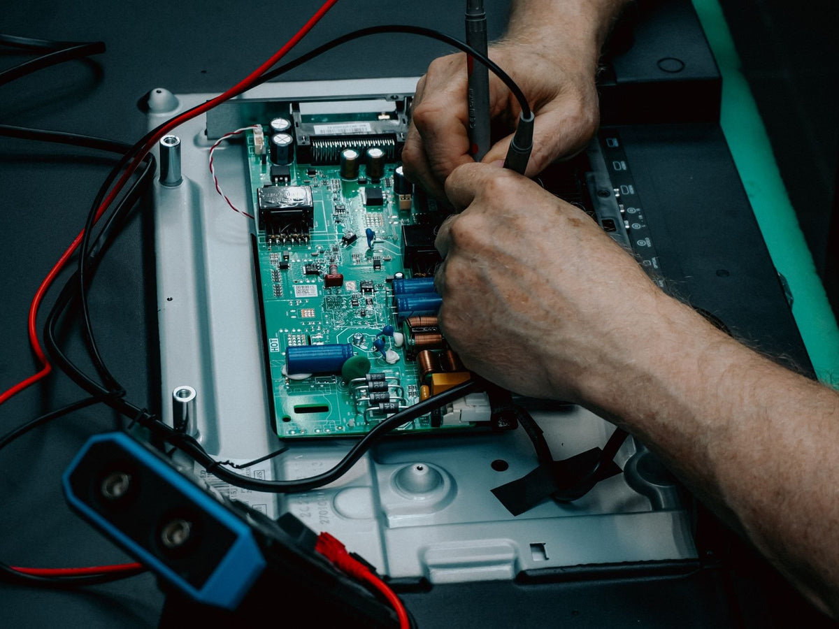 Technician testing a circuit board with a multimeter at a repair bench
